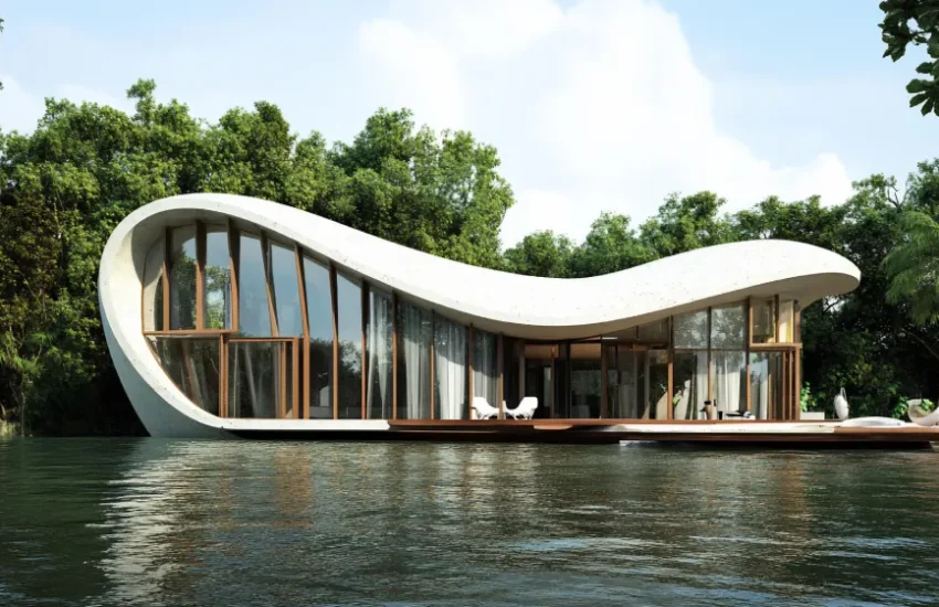 Modern curved houseboat with large glass walls docked on calm water, surrounded by trees.