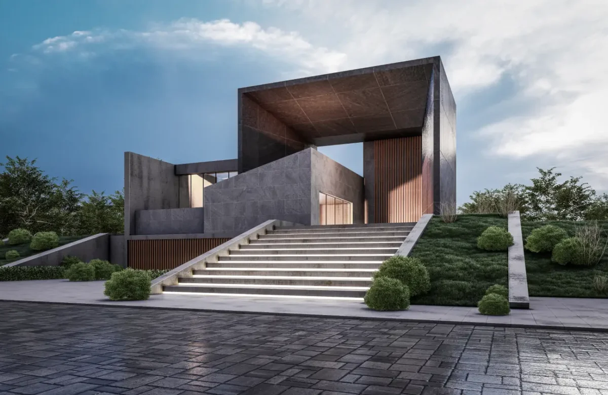 Modern concrete building with a large rectangular frame, reached by illuminated stairs and well-kept landscaping on a sloped site.