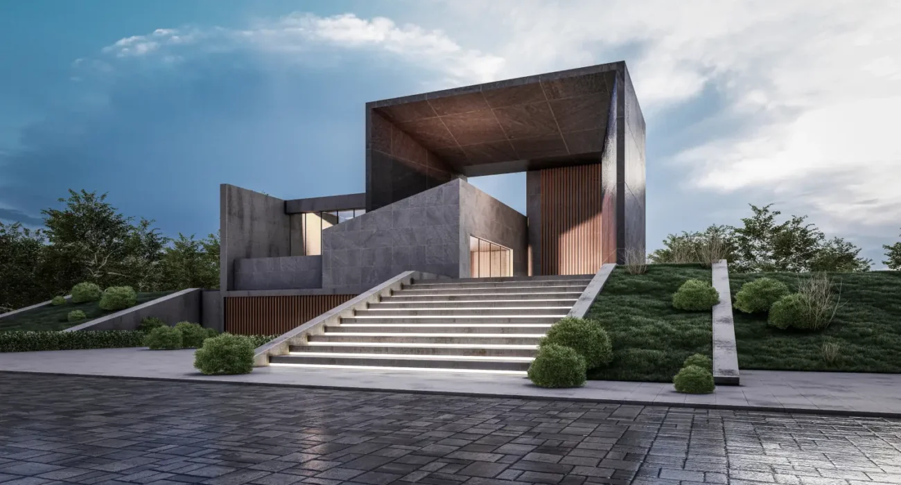 Modern concrete building with a large rectangular frame, reached by illuminated stairs and well-kept landscaping on a sloped site.