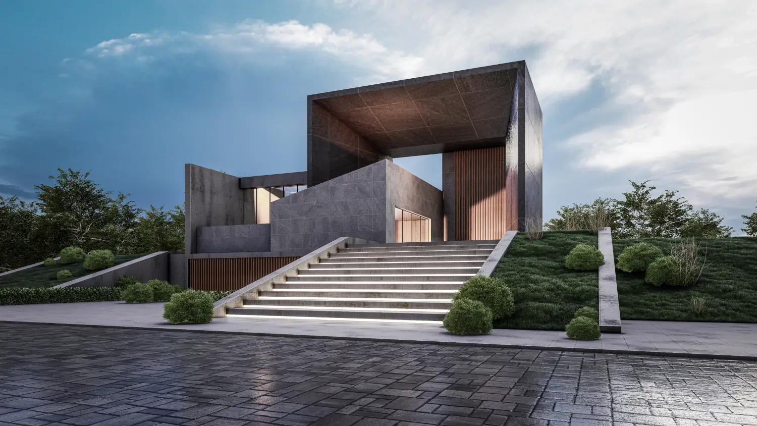 Modern concrete building with a large rectangular frame, reached by illuminated stairs and well-kept landscaping on a sloped site.