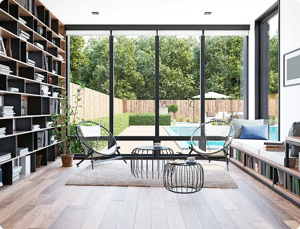 Bright modern living room with floor-to-ceiling glass doors opening to a backyard pool and seating area outside, bookshelves on the left and a cozy rug in the center.