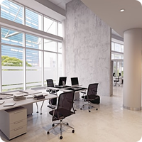 Open-plan office with white desks, black ergonomic chairs, laptops, and large windows flooding the space with daylight.